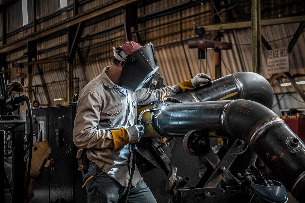 Technician welding steel pipe fittings in an industrial fabrication workshop